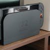 Nintendo console docked among speakers and a monitor on a wooden shelf.